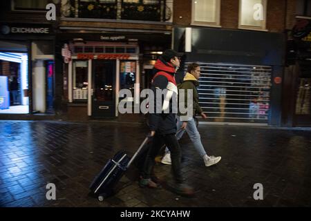 Les touristes avec bagages passent devant les boutiques fermées. Rues d'Amsterdam au cours du premier jour du confinement soudain dans la capitale néerlandaise. La première nation européenne déclare un verrouillage complet pour lutter contre la nouvelle variante d'Omicron qui s'intensifie, les pays-Bas se bloque après que le gouvernement a ordonné la fermeture de tous les magasins, cafés, restaurants, bars, salles de sport, Écoles, lieux sportifs, lieux culturels et autres à partir du dimanche et pendant 4 semaines afin d'empêcher la propagation de la mutation Omicron du coronavirus Covid-19. Amsterdam, pays-Bas sur 19 décembre 2021 (photo de Nicolas Econom Banque D'Images