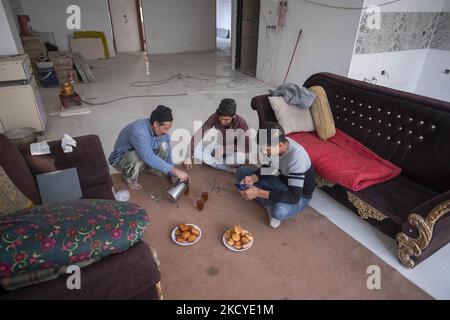 Fereydoun Ahmadi-26 (R), un réfugié afghan et champion du monde de kickboxing, qui doit travailler en tant que travailleur de la construction pour collecter de l'argent pour les frais de subsistance, Utilise son smartphone comme il est assis à côté de ses collègues afghans pendant leur pause dans une pièce d'un immeuble résidentiel en construction, dans la région de Mehrshahr à l'ouest de la ville de Karaj dans la province d'Alborz 53km (33 miles) au nord-ouest de Téhéran sur 10 octobre 2021. Fereydoun est champion du monde de kickboxing et sa femme Masoumeh est également instructeur de kickboxing qui sont tous deux afghans et sont nés en Iran, Banque D'Images