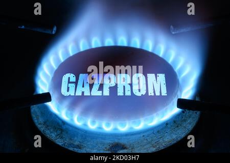 Le gaz brûle dans l'obscurité à la maison, flamme bleue et nom Gazprom sur brûleur à cuisinière. Concept de coût du gaz naturel du gazoduc, chaleur, crise énergétique, économie Banque D'Images