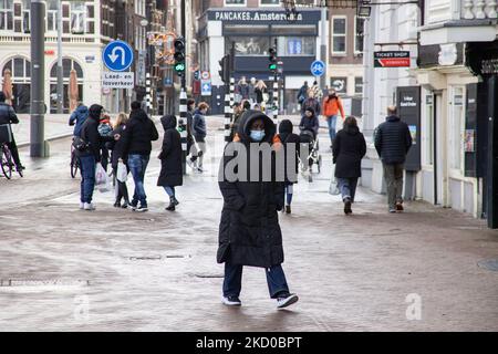 La vie quotidienne dans le centre d'Amsterdam avec quelques personnes portant des masques faciaux. Les habitants et quelques touristes dans les rues calmes d'Amsterdam pendant le confinement dans la capitale néerlandaise avec des magasins et des magasins paraissant avec fermé avec le roller métal volet vers le bas, cafés, bars et restaurants également fermés avec des tables et des chaises des terrasses fermées. Les pays-Bas ont été la première nation européenne à déclarer un verrouillage complet pour lutter contre la nouvelle variante d'Omicron qui s'intensifie. Après une commande soudaine du gouvernement avant Noël, le pays a fermé tous les magasins, cafés, restaurants, bars, salles de sport, écoles Banque D'Images