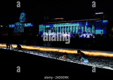 Les enfants portant un masque de protection jouent avec des sables à l'installation d'art intitulée "fragment d'un littoral" comme façade de la Galerie nationale Singapour dans le fond est éclairé par la projection de lumière pendant le Festival lumière-nuit 2022 sur 15 janvier 2022 à Singapour. (Photo de Suhaimi Abdullah/NurPhoto) Banque D'Images