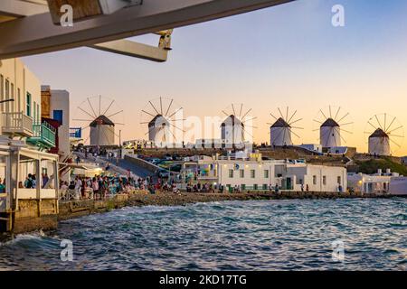 Les moulins à vent emblématiques de l'île de Mykonos vus de la petite Venise avec des touristes dans les bars, cafés et restaurants. Mykonos est une île en Grèce, dans la mer Égée. Il y a 16 moulins à vent sur l'île, dont 5 au-dessus de Chora, la ville principale de l'île. Les moulins à vent ont été construits au 16th siècle à partir des Vénitiens mais leurs constructions se sont poursuivies jusqu'au 20th siècle. Coucher de soleil avec les gens aux moulins à vent de Mykonos. Les touristes apprécient un beau coucher de soleil pendant l'heure magique à l'île de Mykonos en Grèce. L'île grecque de Myconos est une destination de voyage populaire et glamour pour la Méditerranée Banque D'Images