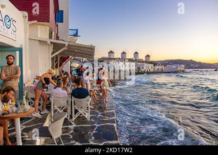 Les moulins à vent emblématiques de l'île de Mykonos vus de la petite Venise avec des touristes dans les bars, cafés et restaurants. Mykonos est une île en Grèce, dans la mer Égée. Il y a 16 moulins à vent sur l'île, dont 5 au-dessus de Chora, la ville principale de l'île. Les moulins à vent ont été construits au 16th siècle à partir des Vénitiens mais leurs constructions se sont poursuivies jusqu'au 20th siècle. Coucher de soleil avec les gens aux moulins à vent de Mykonos. Les touristes apprécient un beau coucher de soleil pendant l'heure magique à l'île de Mykonos en Grèce. L'île grecque de Myconos est une destination de voyage populaire et glamour pour la Méditerranée Banque D'Images