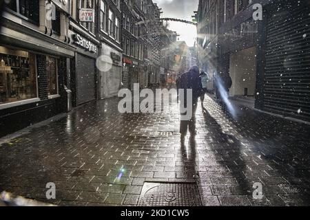 Les gens sont vus comme des silhouettes d'ombre marchant pendant qu'il y a de la pluie et le soleil brille. La vie quotidienne pendant le confinement à la quatrième vague de la pandémie. Les habitants et quelques touristes dans les rues calmes d'Amsterdam pendant le confinement dans la capitale néerlandaise avec des magasins et des magasins paraissant avec fermé avec le roller métal volet vers le bas, cafés, bars et restaurants également fermés avec des tables et des chaises des terrasses fermées. Les pays-Bas ont été la première nation européenne à déclarer un verrouillage complet pour lutter contre la nouvelle variante d'Omicron qui s'intensifie. Après un ordre soudain du gouvernement avant Noël, le cou Banque D'Images