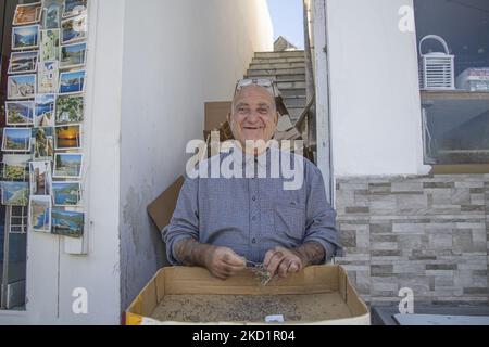 Un homme souriant frotte les herbes séchées des herbes sauvages récoltées et séchées. Livadia, le port et le village principal de l'île de Tilos avec les maisons à l'architecture traditionnelle blanchie à la chaux et la plage avec l'eau de mer cristalline. Telos est une petite île grecque méditerranéenne située dans la partie de la mer Égée des îles Dodécanèse avec une population de 780 habitants près de la côte turque. Fin 2018, Tilos est devenue la première île de la Méditerranée à fonctionner exclusivement sur l'énergie éolienne et solaire, une île verte autosuffisante, une initiative financée par l'UE pour l'énergie verte provenant de sources renouvelables protégeant Banque D'Images