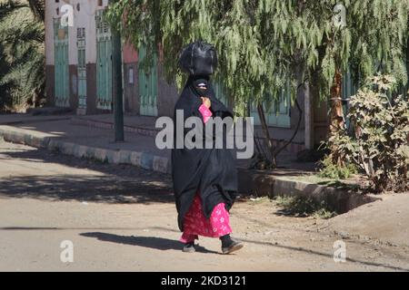 Femme (qui porte un manteau traditionnel noir de corps 'haik') portant un paquet sur sa tête tout en marchant le long d'une route dans un village désertique isolé au fond des montagnes du Haut Atlas au Maroc, en Afrique. (Photo de Creative Touch Imaging Ltd./NurPhoto) Banque D'Images