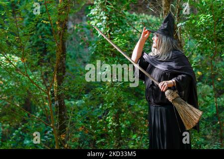 gros plan de sorcière à cheveux blancs avec chapeau en profil dans la forêt avec son balai Banque D'Images