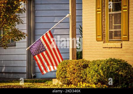 Drapeau américain suspendu vers le bas où le vent a cassé son support contre le fond de la maison au soleil du soir Banque D'Images