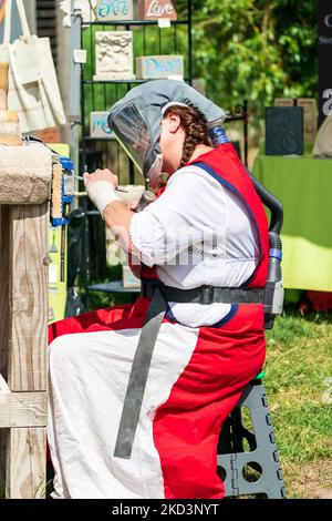 Femme portant un masque de protection avec l'air fourni tout en sculptant et en gravant un morceau de pierre avec burin et marteau, à l'extérieur lors d'un événement. Banque D'Images