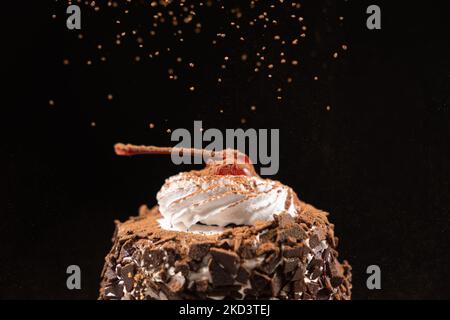 Le cacao est arrosé sur un gâteau au chocolat avec des cerises glacées et de la crème sur fond noir Banque D'Images