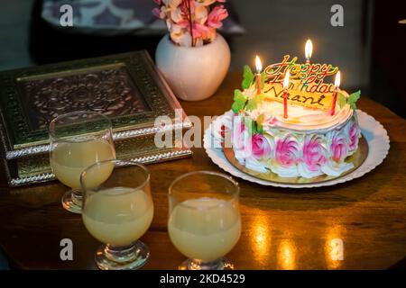 gâteau d'anniversaire de grand-mère maternel décoré de bougies allumées et de verres à jus à table basse Banque D'Images