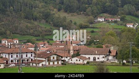 Une ville avec des maisons blanches et des toits rouges dans un champ vert avec des collines et des arbres en arrière-plan Erratzu, Espagne Banque D'Images