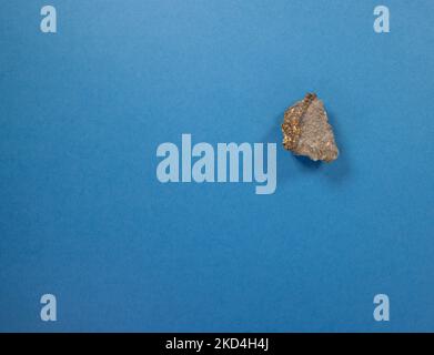 gros plan d'un morceau de roche avec des mouchetures dorées isolées sur un fond bleu foncé Banque D'Images