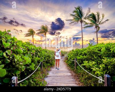 Femme marchant sur le magnifique Beach Path encadré de palmiers menant à la plage, Hollywood Beach, Sunrise Miami, Floride du Sud, États-Unis Banque D'Images