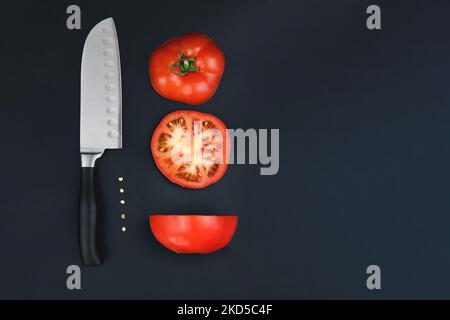 Une tomate coupée en deux moitiés avec un couteau tranchant. Cercles de tomates rouges avec couteau sur fond noir. Récolte de tomates. Concept de nutr sain Banque D'Images