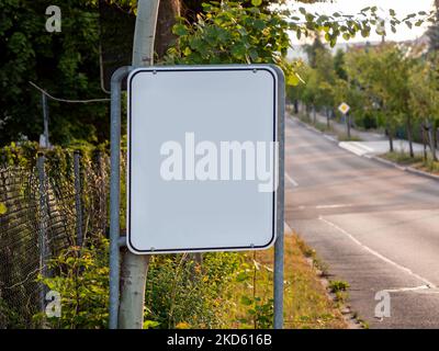 Panneau vide à côté d'une rue. Plaque métallique blanche vierge pour afficher un message d'information aux conducteurs de voiture. La route est vide. Modèle de signalisation routière. Banque D'Images