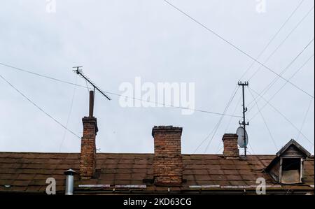 Toit de la vieille maison avec cheminées en briques et fils électriques sur fond de ciel gris Banque D'Images