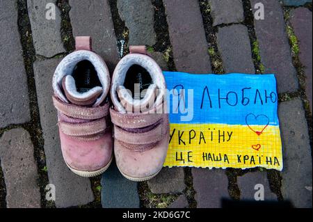 Quelques chaussures pour enfants sont sur le sol, près d'un écriteau pour soutenir l'Ukraine, Une femme met des chaussures pour enfants sur le sol, Dans le cadre d'une installation d'art ukrainienne pour attirer l'attention sur les meurtres de civils et en particulier d'enfants pendant la guerre en Ukraine. La Haye, sur 2 avril 2022. (Photo par Romy Arroyo Fernandez/NurPhoto) Banque D'Images