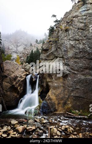 Un cliché vertical d'une petite cascade entourée de rochers dans une montagne brumeuse Banque D'Images