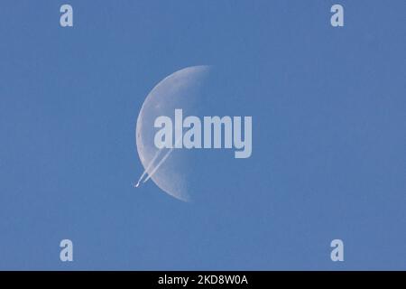 Un avion de passagers navigue à 40,000 pieds d'altitude et passe devant la demi-lune, un jour de printemps sans nuages, tandis que l'avion vole au-dessus de l'Europe dans le ciel hollandais. Moonpass est le but ultime des photographes d'aviation, les planespotters. Pendant le vol, le jet passager laisse derrière lui des contrailles ou un sentier de condensation, une ligne de vapeur blanche qui passe devant le satellite naturel de la Terre et l'objet céleste le plus proche de l'univers. Eindhoven, pays-Bas sur 24 avril 2022. (Photo de Nicolas Economou/NurPhoto) Banque D'Images