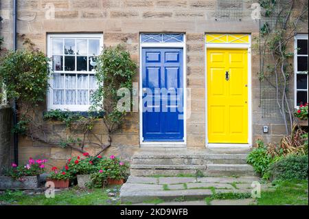 Portes avant peintes en bleu et jaune sur les maisons en terrasse. Chalets de vacances, Robin Hoods Bay, Yorkshire, Royaume-Uni Banque D'Images