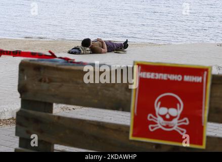 Un homme se repose sur la plage derrière le panneau de mise en garde qui lit « colère, mines » à Odesa, en Ukraine, le 24 mai 2022. La saison des plages à Odesa est généralement considérée comme ouverte à la fin du mois de mai, mais en 2022 elle est sous la menace de l'invasion de l'Ukraine par la Russie. Les policiers marchent le long des plages et demandent aux vacanciers de quitter la côte pour des raisons de sécurité. (Photo par STR/NurPhoto) Banque D'Images