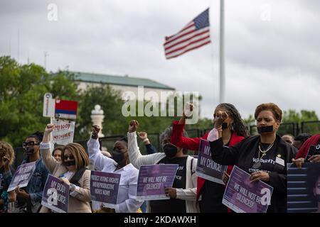 Un drapeau américain vole à la moitié du personnel à l'extérieur de la Cour suprême à Washington, D.C., sur 25 mai 2022, un jour après une fusillade de masse dans une école à Uvalde, Texas, alors que les femmes tiennent leurs poings dans les airs lors d'un rassemblement et d'une protestation silencieuse exigeant des droits de reproduction et de vote (Photo de Bryan Olin Dozier/NurPhoto) Banque D'Images