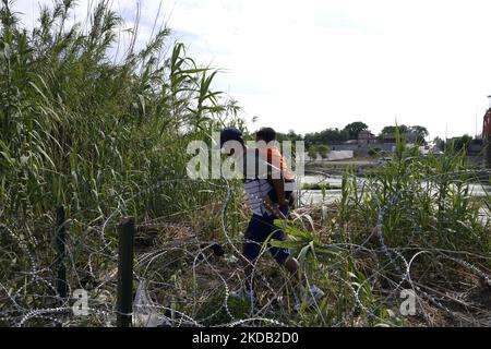 Les migrants, la plupart avec des enfants suivent un chemin le long du fil de la concertina où ils seront placés sous la garde par la patrouille frontalière après avoir traversé le Rio Grande sur 27 mai 2022 à Eagle Pass Texas, États-Unis. Titre 42, le mandat de l'ère Trump qui a été fixé pour empêcher les migrants d'entrer aux États-Unis, Devait expirer sur 23 mai mais a été bloqué par une poursuite déposée par plusieurs États citant que la décision d'attaquer la loi "n'a pas satisfait aux normes fixées par la Loi sur la procédure administrative" et qu'il n'y a pas de solution permanente pour gérer l'inévitable augmentation de l'immigration. Les opposants à la défense de Banque D'Images