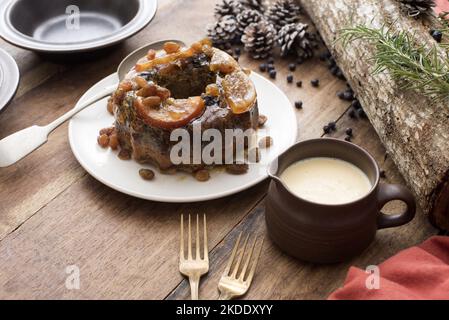 Un petit pudding de prune avec crème au brandy ou sauce prête à être servi pour le dessert de Noël sur une table en bois décorée Banque D'Images