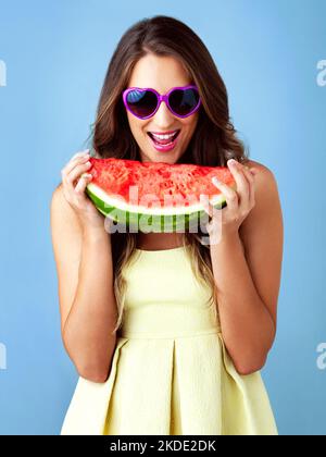 Il est difficile de ne pas être heureux de manger une pastèque. Photo studio d'une belle femme tenant une pastèque sur fond bleu. Banque D'Images