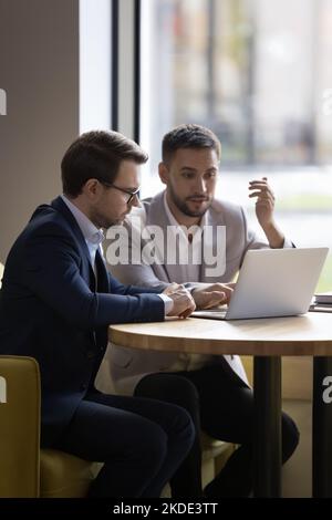 Deux jeunes collègues de bureau de 35s ans discutent de l'utilisation en ligne d'un ordinateur portable Banque D'Images