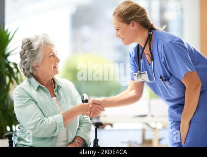 C'est super de vous rencontrer enfin. Une infirmière féminine attirante se serrant la main avec son patient senior attaché à la roue à l'hôpital. Banque D'Images