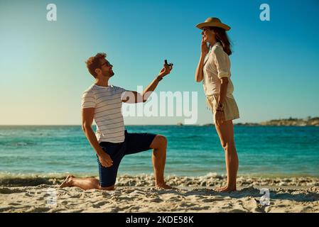 L'endroit idéal pour un séjour d'été. Un jeune homme propose à sa petite amie à la plage le jour de l'été. Banque D'Images
