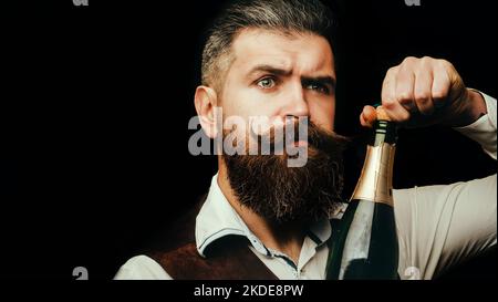 Portrait d'un serveur barbu tenant une bouteille de champagne. Gros plan portrait d'un homme qui a déballé une bouteille de champagne. Champagne. Homme en fête Banque D'Images