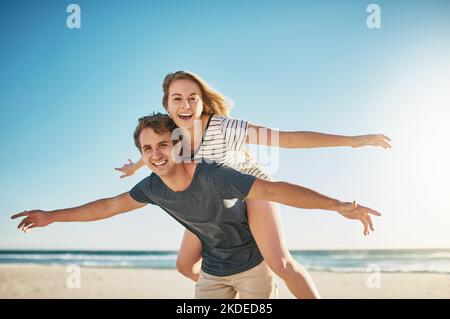 La liberté, c'est vivre une vie remplie d'amour. Un jeune couple heureux qui profite d'une promenade en pigeyback à la plage. Banque D'Images