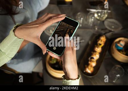Une blogueuse de l'alimentation photographie des plats asiatiques avec son téléphone mobile tout en encadrant une assiette de dim sum vapeur pour ses réseaux sociaux - nourriture et boissons et te Banque D'Images