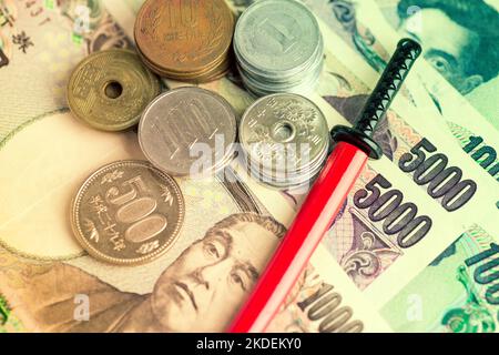 Editorial tonique illustrant le yen japonais en notes et pièces de monnaie et un katana miniature en barde rouge. Banque D'Images