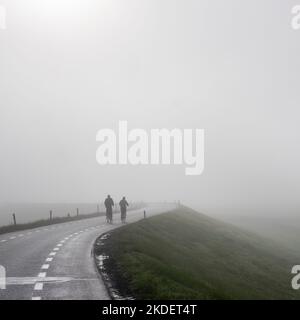 couple sur des balades à vélo dans la brume sur la digue près du rhin en hollande Banque D'Images