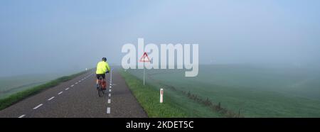 homme sur des balades à vélo dans la brume sur la digue près du rhin en hollande Banque D'Images