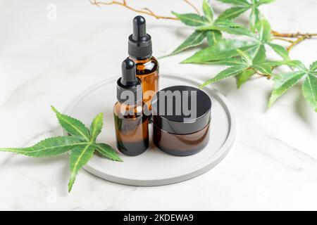 Bouteilles en verre avec de l'huile de CBD, teinture de THC et feuilles de chanvre sur plateau un fond de marbre. Cosmétiques huile et crème de cannabis Banque D'Images