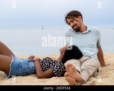 Hétérosexuels divers jeunes couples assis affectueusement en face de la mer Banque D'Images