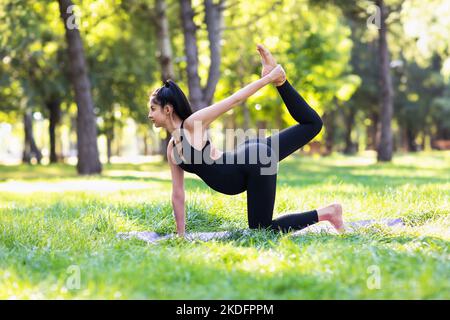 Jeune femme enceinte menant un mode de vie sain et pratiquant le yoga, exécute l'exercice Ardha Dhanurasana, la pose semi-cercle, des trains dans le parc sur Banque D'Images