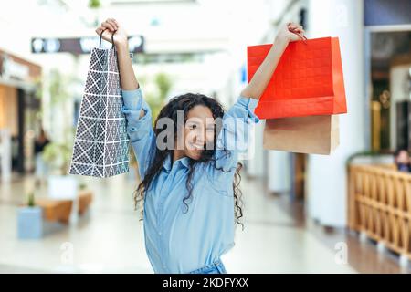 Bonne cashopper femme regardant l'appareil photo et souriant, hispanique femme avec la danse des cheveux bouclés et le saut avec plaisir, a acheté des cadeaux en vente, portrait de la bonne femme de shopping. Banque D'Images