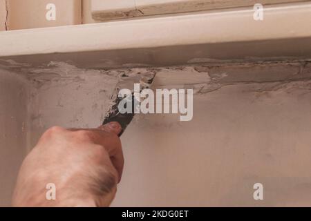 Homme main enlever la vieille peinture d'un mur à l'aide d'une spatule en métal. Concept de rénovation, fait maison. Copier l'espace Banque D'Images