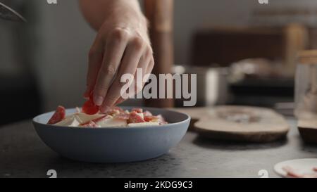 ajouter les tomates cerises aux pâtes fusilli dans un bol bleu, photo large Banque D'Images