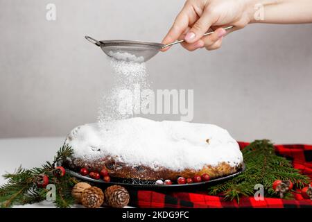 La main d'une femme saupoudrer la poudre à travers un tamis sur un stollen allemand de Noël Banque D'Images