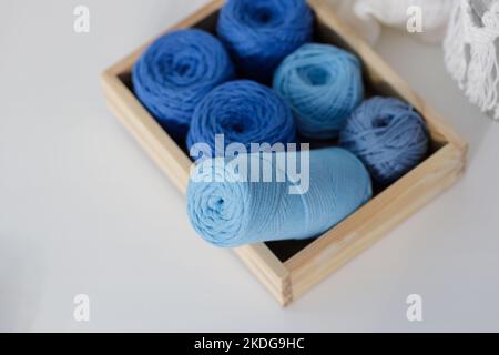 Boules de cordes en coton macrame bleu et bleu clair dans une boîte en bois sur une table blanche Banque D'Images