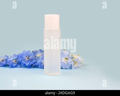 Bouteille d'eau micellaire claire et fleur de delphinium bleue sur fond bleu. Lotion pour le nettoyage de la peau à partir de cosmétiques, maquillage. Produit de beauté liquide Banque D'Images