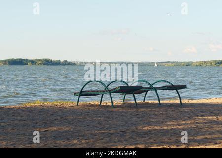 Chaises longues sur le rivage sablonneux du lac dans les rayons du soleil couchant. Banque D'Images