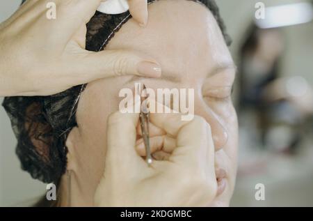 Les mains du styliste plisent les sourcils avec une pince à épiler sur le visage d'une femme. Gros plan. Soins du visage. Banque D'Images